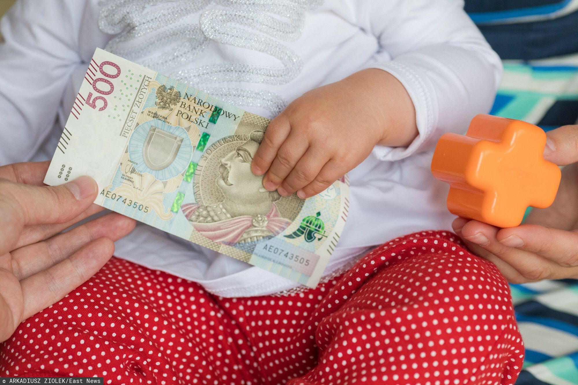 fot: Arkadiusz Ziolek/ East News. 16.07.2019. n/z Dlon dziecka i matki na tle zabawek i banknotu 500 zl.