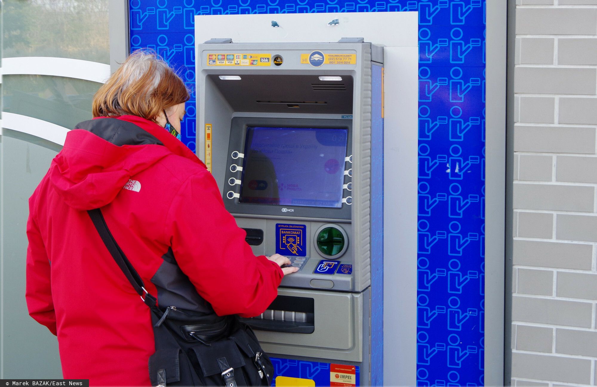 Kobieta wypłaca środki pieniężne z bankomatu - materiał ilustracyjny